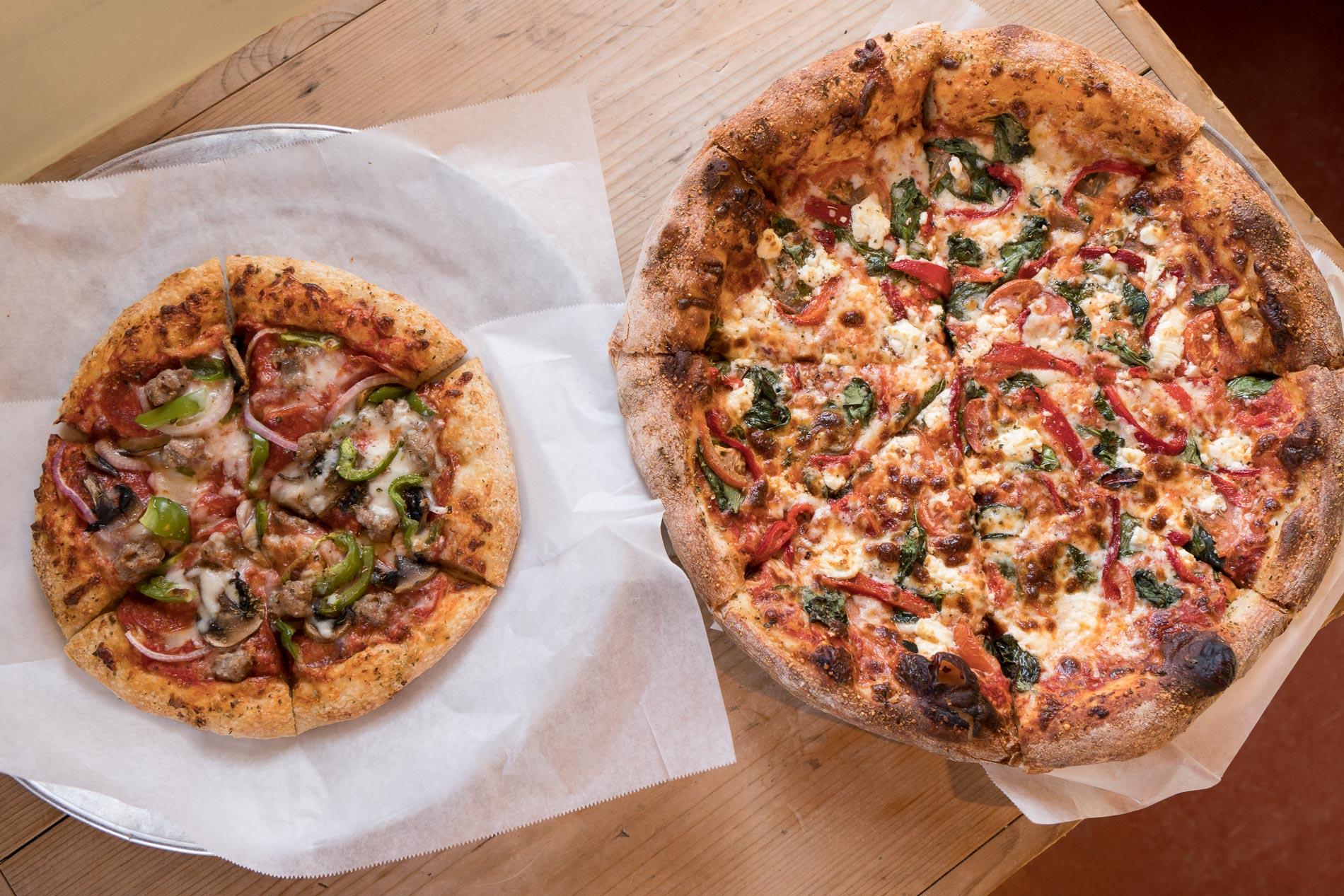 Two different sized pizzas with variety of toppings in restaurant in Monhegan Maine.